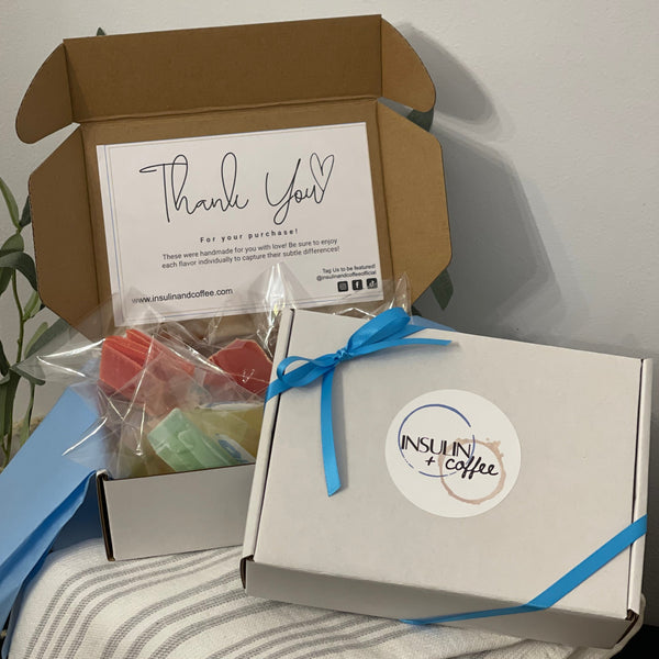 MonkGems are a sugar free crystal gummy candy. Gift box packaging showing how candies are wrapped in a blue ribbon box with logo sticker on the front against light background with a gray wall on a gray striped towel.